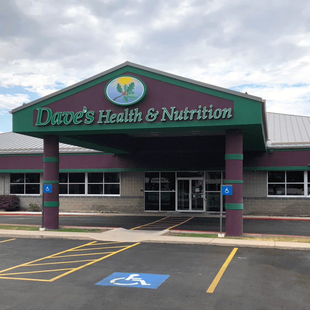 Dave's Health and Nutrition store. Purple building with some green borders. The name is in green. Cloudy sky behind building. Some parking stalls in front.