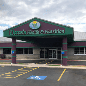 Dave's Health and Nutrition store. Purple building with some green borders. The name is in green. Cloudy sky behind building. Some parking stalls in front.